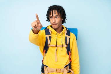 Genç dağcı Afrikalı Amerikalı büyük sırt çantalı adam mavi arka planda izole edilmiş şeffaf ekrana dokunuyor.