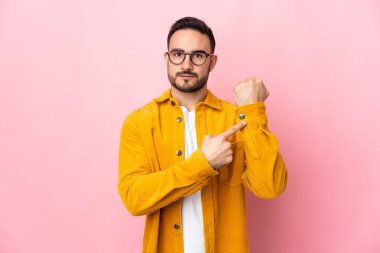 Pembe arka planda izole edilmiş beyaz, yakışıklı bir adam geç kalma jesti yapıyor.