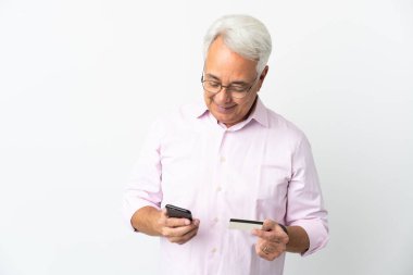 Orta yaşlı Brezilyalı bir adam beyaz arka planda izole edilmiş cep telefonuyla kredi kartıyla alışveriş yapıyor.