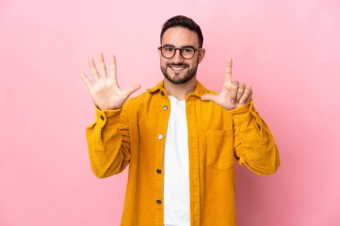 Pembe arka planda izole edilmiş beyaz tenli yakışıklı adam yediyi parmaklarıyla sayıyor.