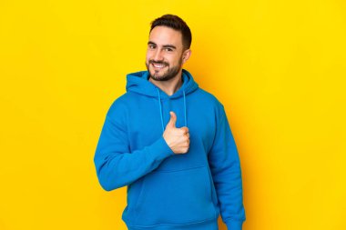 Sarı arka planda izole edilmiş beyaz, yakışıklı genç bir adam baş parmak işareti yapıyor.