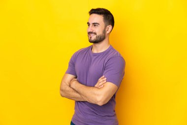 Sarı arka planda izole edilmiş, kolları bağlı ve mutlu, beyaz, yakışıklı genç bir adam.