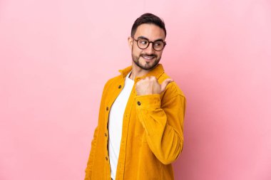 Pembe arka planda izole edilmiş beyaz, yakışıklı genç bir adam bir ürün sunmak için kenarı işaret ediyor.