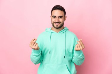 Beyaz tenli yakışıklı adam pembe arka planda izole edilmiş para hareketi yapıyor.