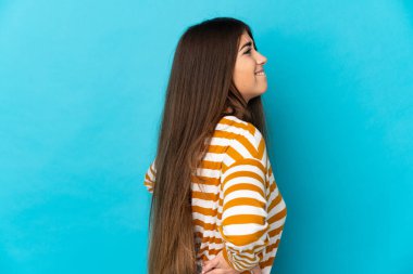 Genç, beyaz bir kadın, mavi arka planda izole edilmiş. Çaba gösterdiği için sırt ağrısı çekiyor.