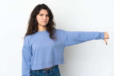 Beyaz arka planda izole edilmiş genç bir Rus kızı, olumsuz ifadeyle baş parmağını aşağı gösteriyor.