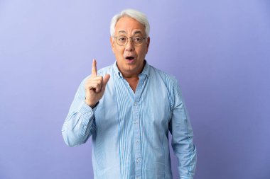 Orta yaşlı Brezilyalı adam mor arka planda izole edilmiş bir şekilde parmağını kaldırarak çözümü bulmaya çalışıyor.