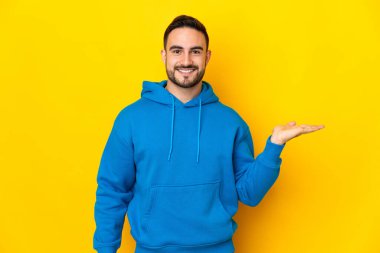 Beyaz, yakışıklı, sarı arka planda izole edilmiş genç bir adam. Avucunun içinde hayali bir fotokopi makinesi tutuyor.