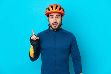 Genç bisikletçi, mavi arka planda izole edilmiş bir şekilde parmağını kaldırarak çözümü bulmaya çalışıyor.