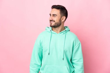 Pembe arka planda soyutlanmış beyaz tenli yakışıklı bir adam. Yan tarafa bakıyor ve gülümsüyor.