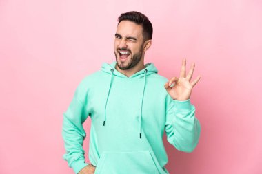 Pembe arka planda izole edilmiş beyaz, yakışıklı genç bir adam parmaklarıyla tamam işareti gösteriyor.