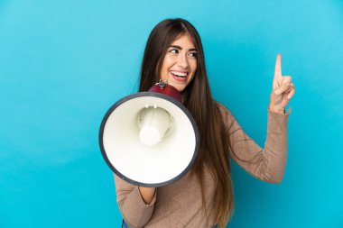 Mavi arka planda izole edilmiş genç beyaz kadın megafonla bağırıyor ve işaret ediyor.