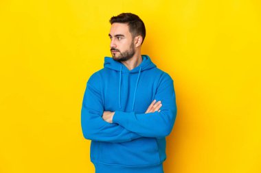 Sarı arka planda izole edilmiş beyaz, yakışıklı genç bir adam kollarını kavuşturuyor.