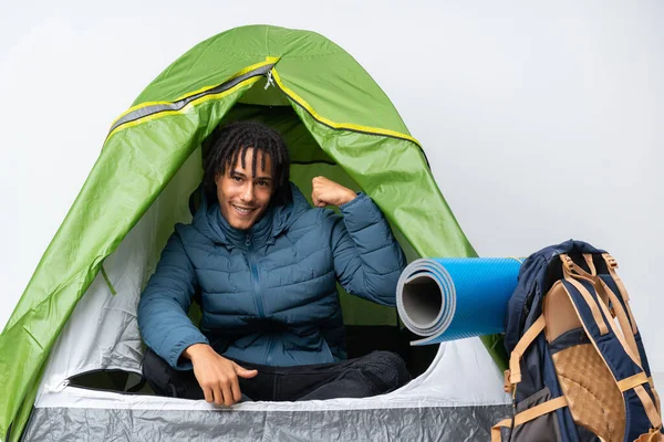 Young african american man inside a camping green tent doing strong gesture