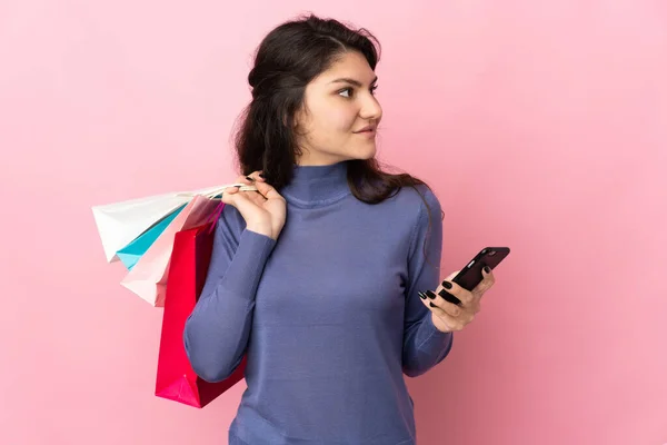 ティーネージャーロシアの女の子孤立した上ピンクの背景保持ショッピングバッグと携帯電話 — ストック写真