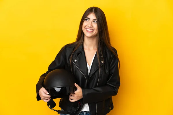 若いですCaucasian女性を保持していますオートバイヘルメット隔離上の黄色の背景思考アイデア上を見ながら — ストック写真