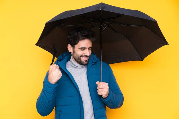 勝利を祝う黄色の背景に傘を持っている男 — ストック写真