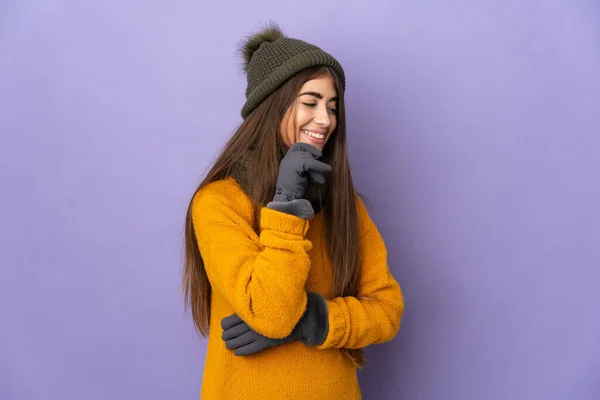年轻的高加索女孩 头戴冬季帽 背景紫色 望着侧面 面带微笑 — 图库照片