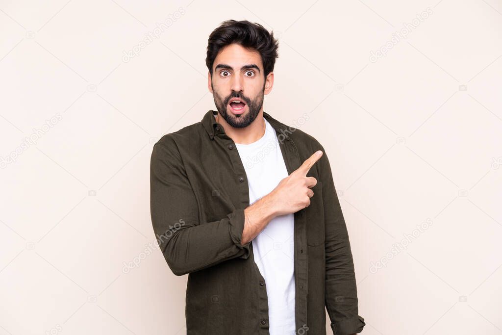 Young handsome man with beard over isolated background surprised and pointing side