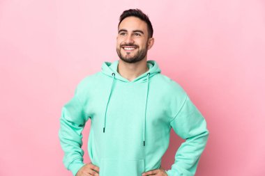 Beyaz tenli yakışıklı, pembe arka planda soyutlanmış, kolları kalçasında ve gülümsüyor.