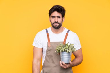 Bahçıvan sakallı, izole edilmiş sarı arka planda şüpheleri olan ve kafası karışık bir yüz ifadesi olan bir adam.