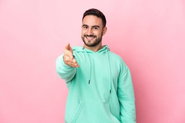 Beyaz tenli yakışıklı adam pembe arka planda izole edilmiş ve iyi bir anlaşma için el sıkışıyor.