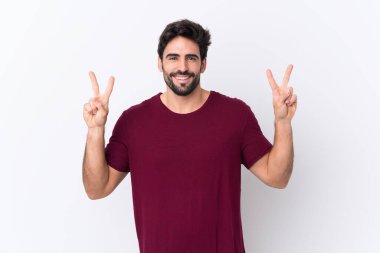 Sakallı yakışıklı genç adam izole edilmiş beyaz arka planda iki eliyle zafer işareti gösteriyor.