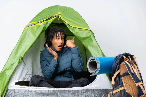 Young african american man inside a camping green tent making phone gesture and doubting