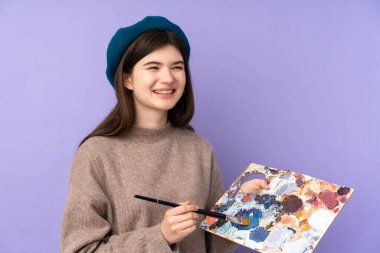 İzole edilmiş mor arka plan üzerinde palet tutan Ukraynalı genç sanatçı kız