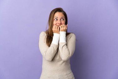 Orta yaşlı Brezilyalı bir kadın mor arka planda izole edilmiş gergin ve korkmuş bir şekilde elleriyle suni teneffüs yapıyor.