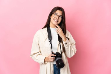 Genç fotoğrafçı Brezilyalı kız pembe arka planda izole edilmiş gülümserken yukarı bakıyor