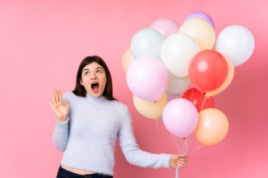 Genç Ukraynalı genç kız, pembe arka planda bir sürü balon tutuyor ve sürpriz bir yüz ifadesi var.