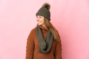 Pembe arka planda izole edilmiş kış şapkalı orta yaşlı kadın.