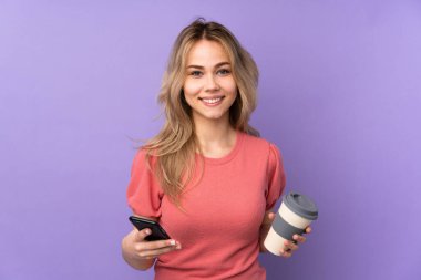 Mor arka planda izole edilmiş genç bir Rus kız elinde kahve ve cep telefonu var.