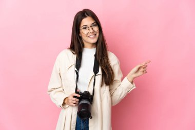 Genç fotoğrafçı Brezilyalı kız pembe arka planda izole edilmiş, parmağıyla kenarı işaret ediyor.