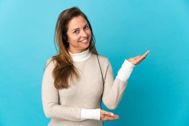 İzole edilmiş mavi arka planda genç bir pazarlamacı kadın davet edildiği için ellerini yana uzatıyor.