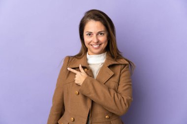 Mor arka planda izole edilmiş orta yaşlı Brezilyalı kadın bir ürünü sunmak için kenarı işaret ediyor.