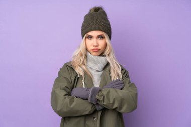 Kışlık şapkalı genç sarışın kız mor arka planda kendini üzgün hissediyor.