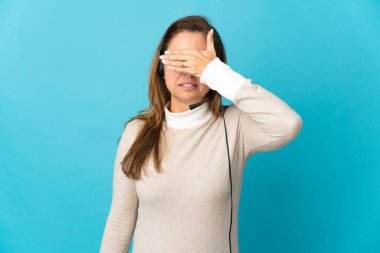 İzole edilmiş mavi arka planı olan genç pazarlamacı kadın elleriyle gözlerini kapatıyor. Bir şey görmek istemiyorum.