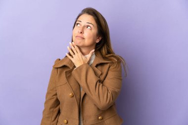 Orta yaşlı Brezilyalı kadın mor arka planda izole edilmiş gülümserken yukarı bakıyor