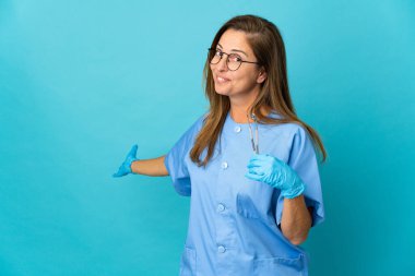 Orta yaşlı Brezilyalı kadın izole edilmiş arka planda aletleri tutuyor. Davet etmek için ellerini yana uzatıyor.