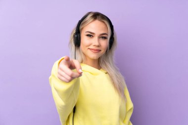 İzole edilmiş mor arka planda müzik dinleyen ve ön tarafı gösteren genç bir kız.