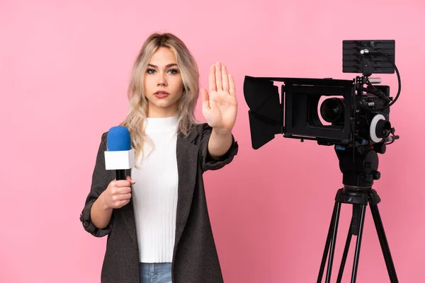 Reporter woman holding a microphone and reporting news over isolated pink background making stop gesture