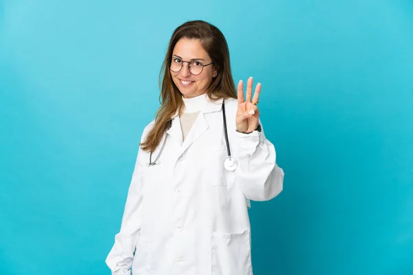 巴西中年妇女医生快乐地与蓝色背景隔离 用手指数着三个 — 图库照片