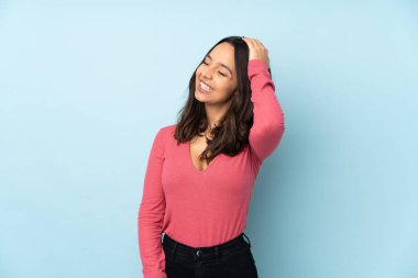 Genç melez kadın mavi arka planda izole edilmiş, çok gülümsüyor.