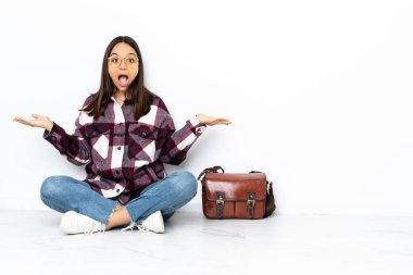 Yüzünde şok ifadesi olan genç bir bayan öğrenci yerde oturuyor.