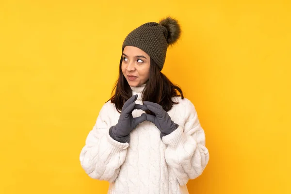 一个戴着冬帽的年轻女子在孤零零的黄色背景下密谋着什么 — 图库照片