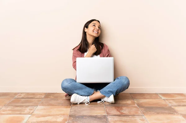 年轻的混血女子 带着笔记本电脑坐在地板上 面带微笑地抬起头来 — 图库照片