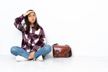 Genç bayan öğrenci yerde oturuyor ve yan tarafa bakarken sürpriz jest yapıyor.