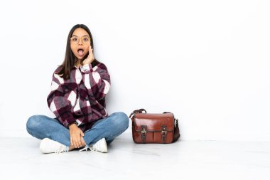 Genç bir bayan öğrenci, şaşkınlık ve şok olmuş bir yüz ifadesiyle yerde oturuyor.